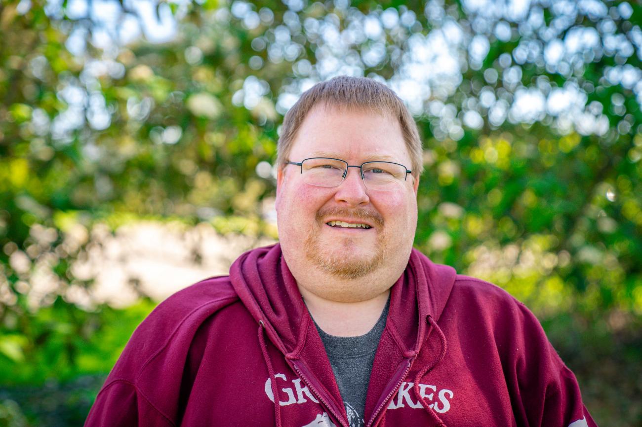 A white man with short hair glasses and wearing a red hoodie smiles at the camera.