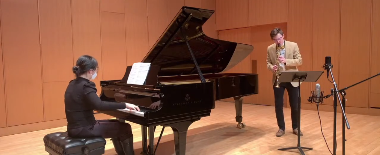 Noah, a young white man, plays a brass instrument with a large grand piano accompaniment