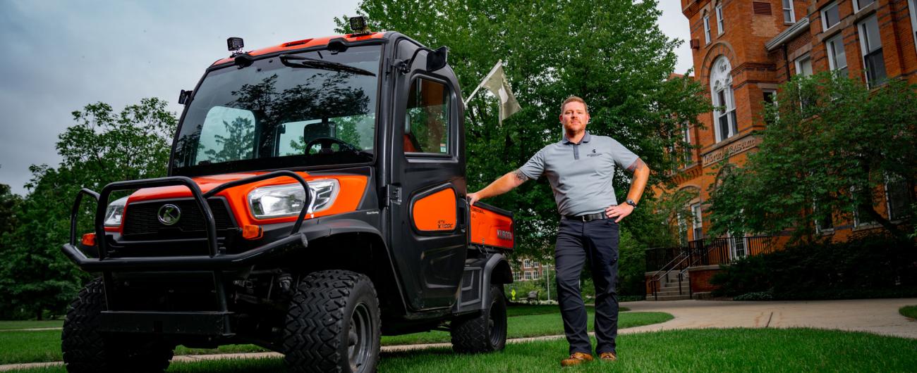 Josh Ridner stands next to an orange Kubota utility vehicle in front of the MSU Museum.