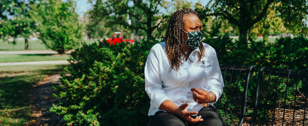 Kisha in a white IPF shirt sits on a bench in a shady area.