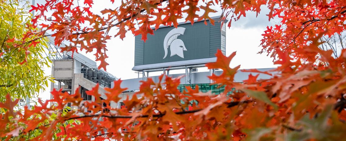 The large stadium sign with the Spartan helmet seen through vibrant orange leaves