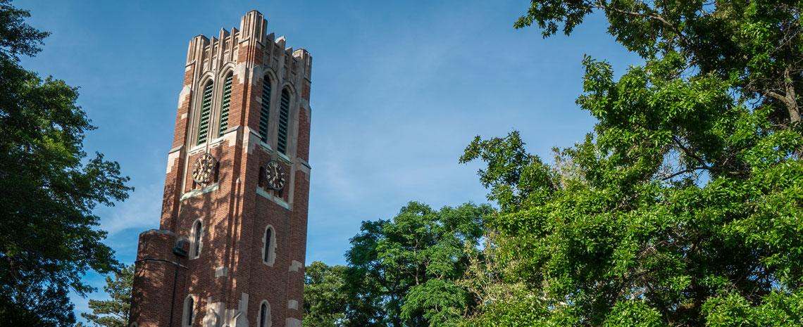 Beaumont tower stands tall in front of a blue sky with green-leafed trees all around