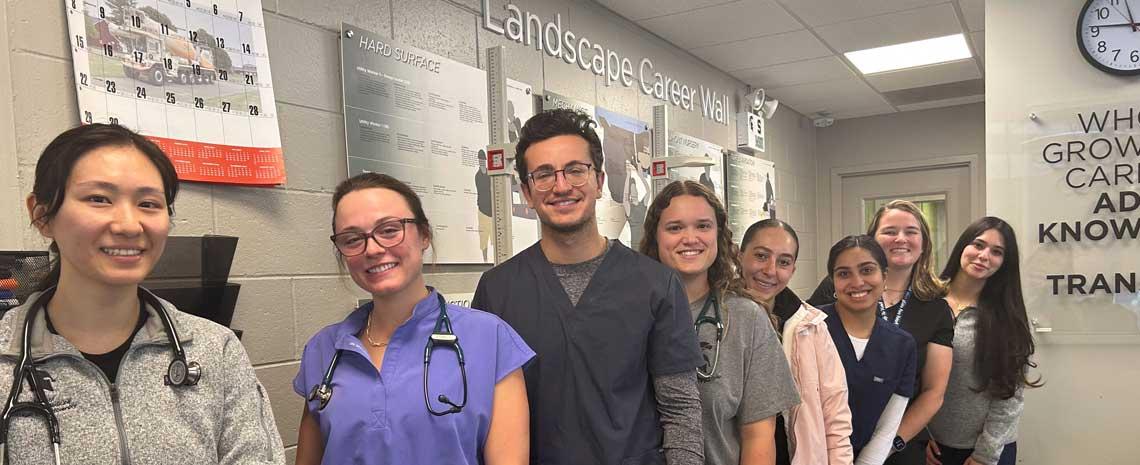 College of Osteopathic medicine students smile in front of the Landscape Services career wall