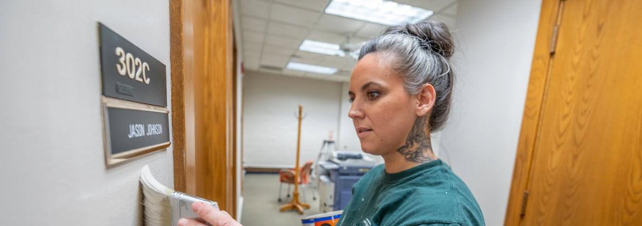 Jessica Woolum hand paints a wall outside of an office