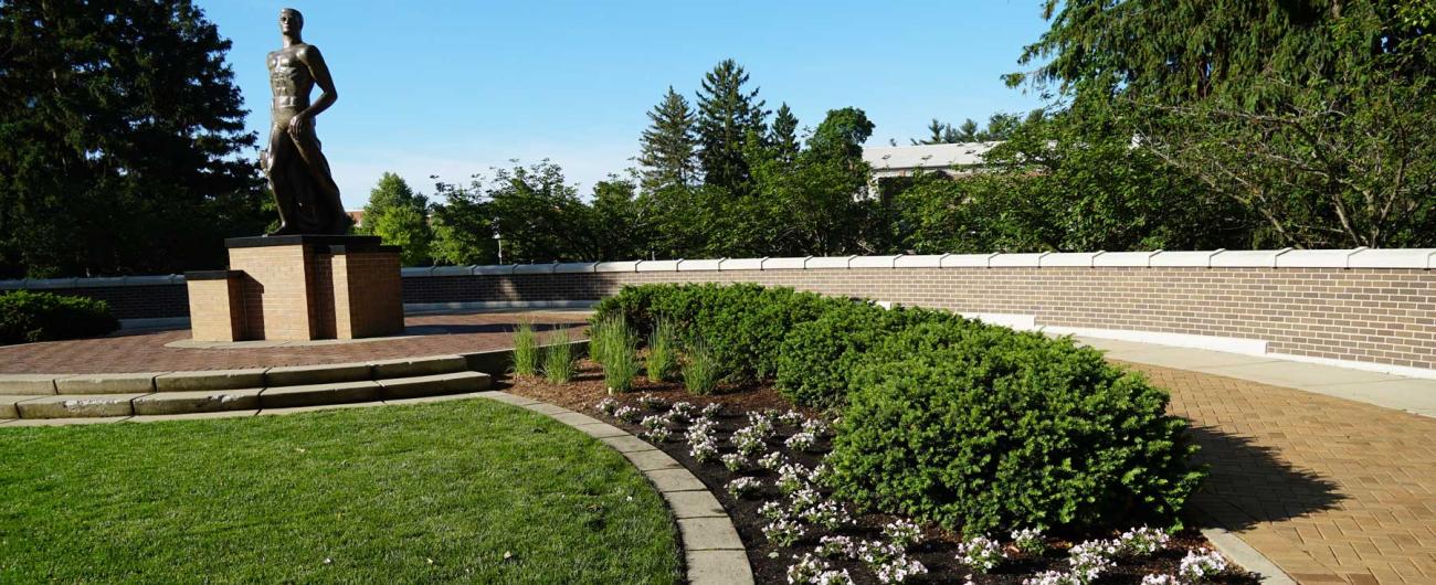 Spartan statue surrounded by green grass and planted flowers