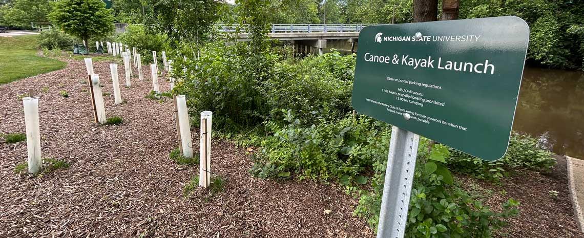 Red Cedar River with a sign in the foreground reading Canoe and Kayak launch