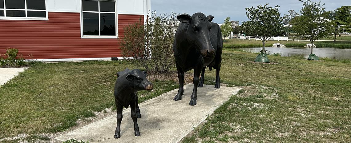 A bronze cow and calf stand together surrounded by green lawns.