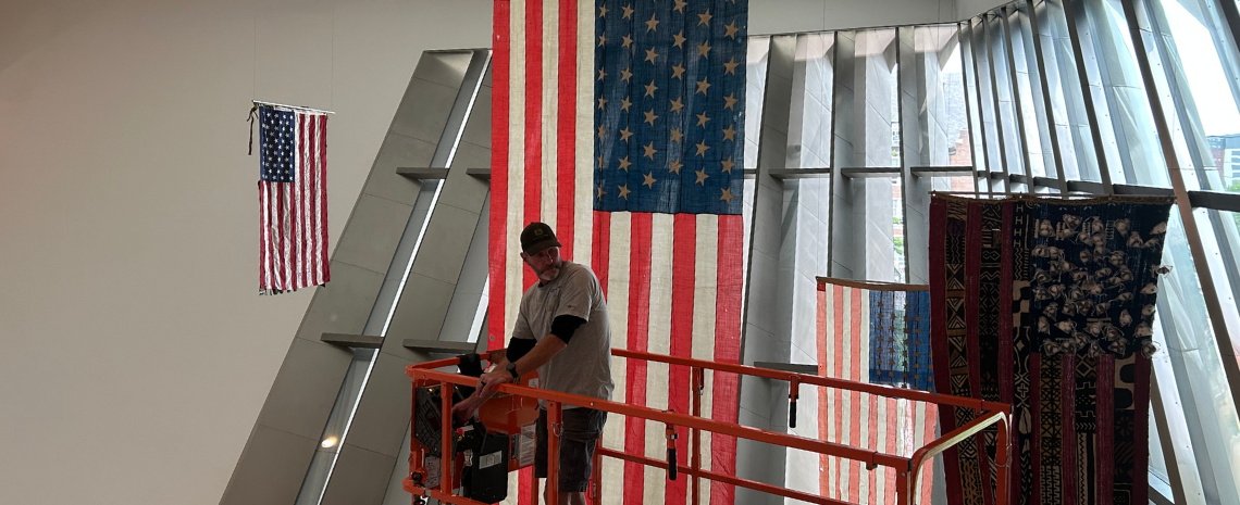 A IPF team member on a raised lift works on a flag hanging from the ceiling.